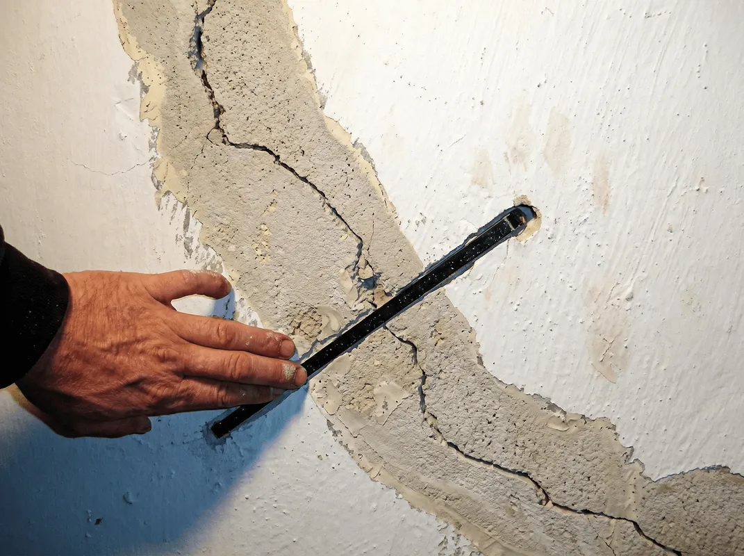 A wall with a large crack is being inspected by a professional in Fresno, CA
