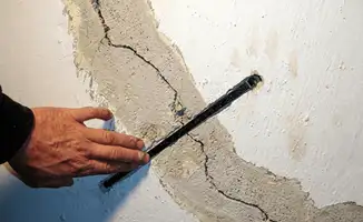 A wall with a large crack is being inspected by a professional in Fresno, CA